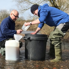 two men filtering water through plastic bins in a river 