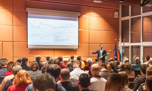 A man presenting in front of a seminar room full of people.