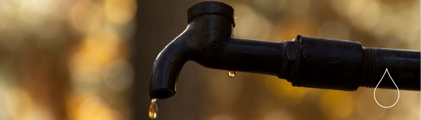 Close up of a water droplet dripping from an outdoor water faucet