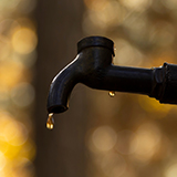 Close up of a water droplet dripping from an outdoor water faucet