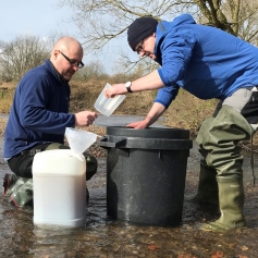 two researchers with bins looking for plastic in a river
