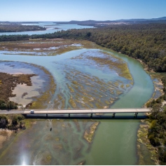 aerial view of a river flowing under a bridge surrounded by forest