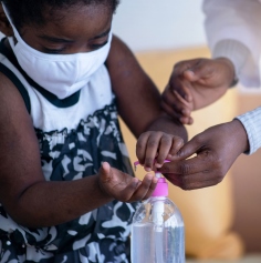 A child wearing a PPE mask taking hand sanitiser out of a bottle 