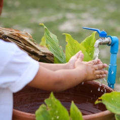 A child washing their hands in an outdoor water tap